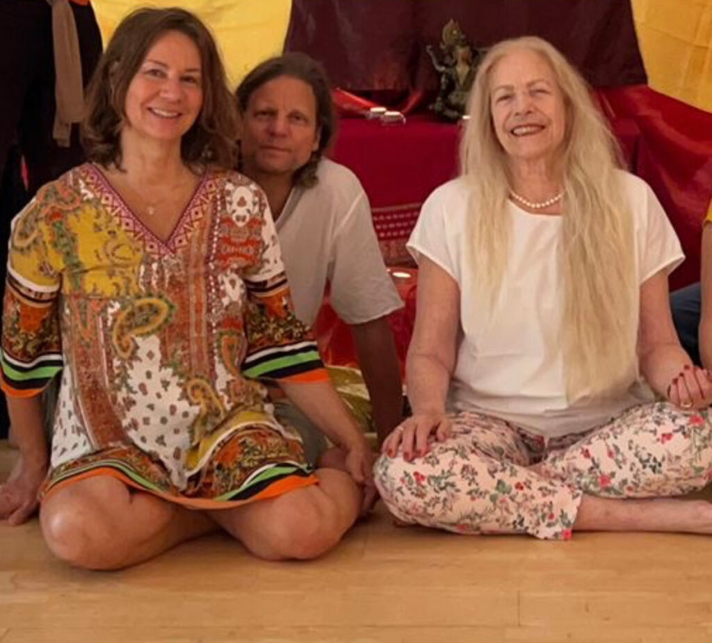 Martina Christian und Advaita sitzen lächelnd auf dem Boden in einem Seminarraum